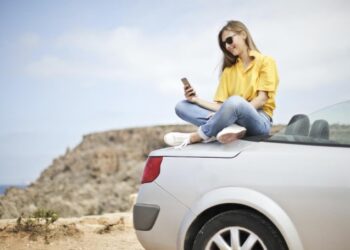 Chica sentada sobre coche descapotable con movil